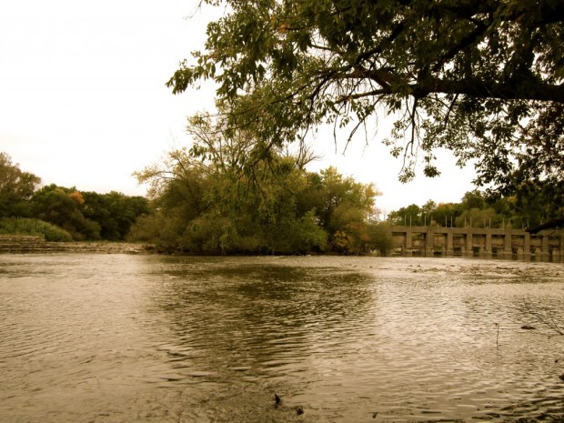 The Federal government claims to own the small island in the center of this photo. The island divides the Estabrook Park dam's gated channel (at right) and the dam's low serpentine spillway (at left). How this man-made island became Federal property is unclear. Photo by Carl Swanson