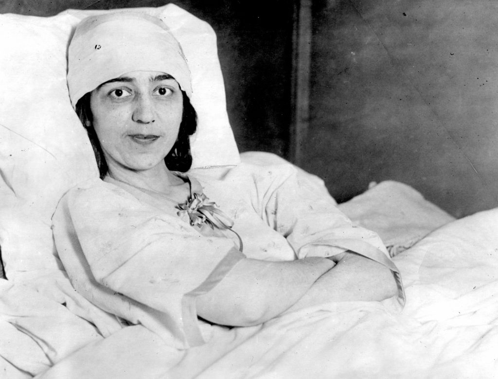 1923 photograph of long-term fever sufferer Anne Manthie of Milwaukee, depicted smiling slightly, with her head bandaged, and propped up in bed.
